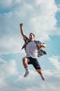 A joyful young man jumps midair with clouds and blue sky in the background, exuding energy and freedom.